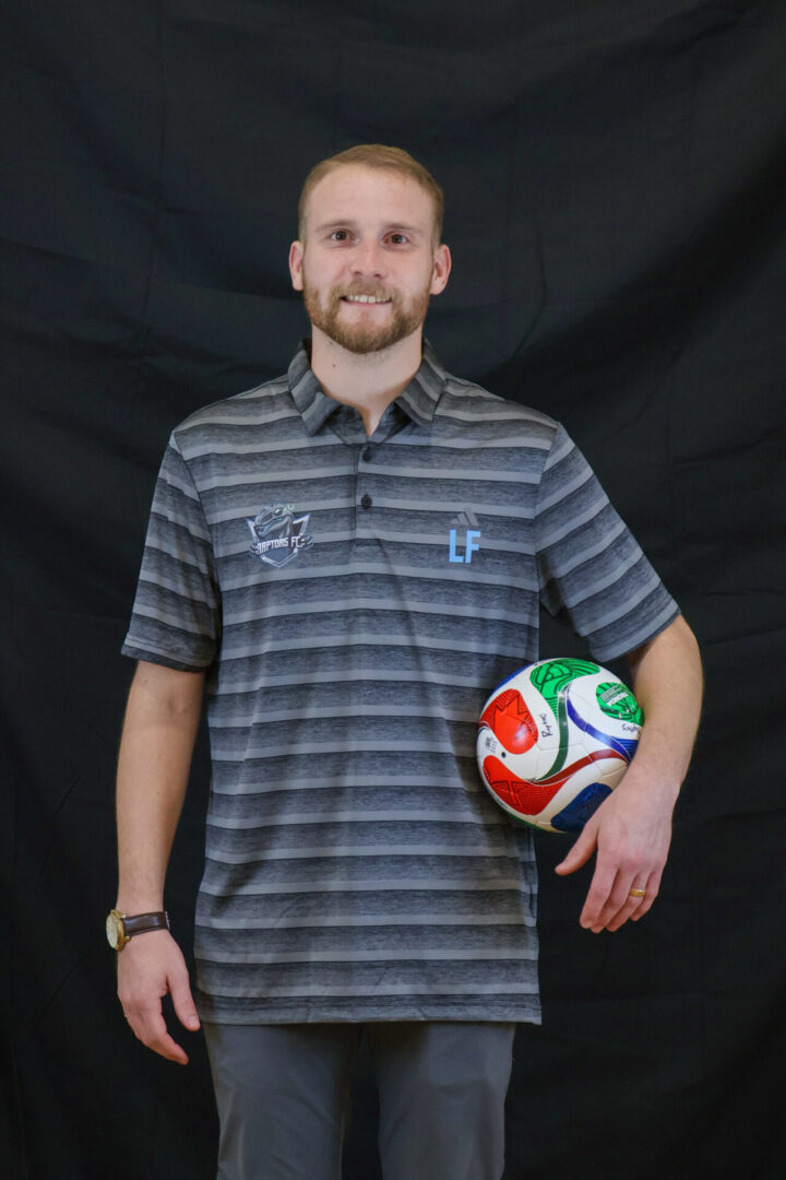 A man in a striped polo shirt holding a colorful soccer ball.